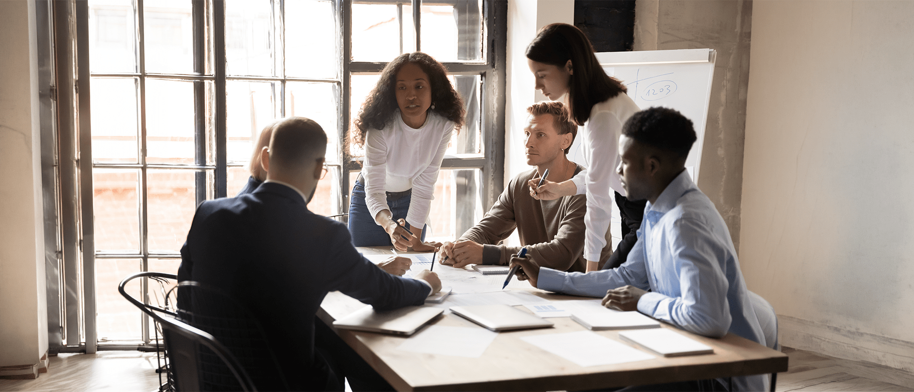 A diverse group of five professionals collaborate over documents in a bright, modern meeting room, discussing ideas and strategies.